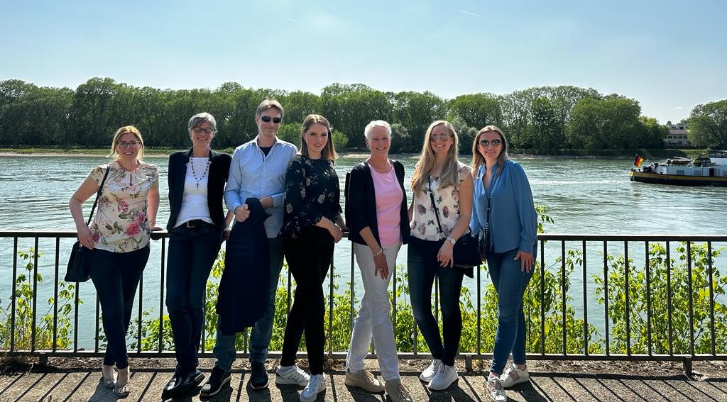 Foto zeigt Teammitglieder der PULSAR Medical AG, die das 3-jährige Jubiläum von PULSAR Medical AG feiern. Die Teammitglieder stehen in einer Reihe vor einem Zaun, dahinter ist ein See zu sehen mit einem Schiff. Die Sonne scheint und alle Teammitglieder sind am lächeln.