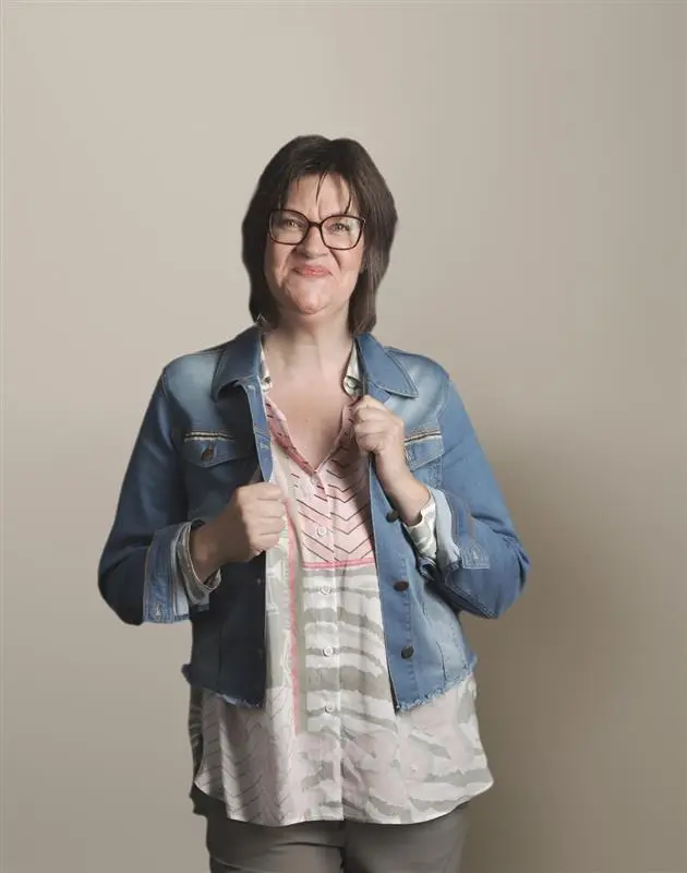 Frau mit Brille und Jeansjacke, die lächelt und die Jacke hält.