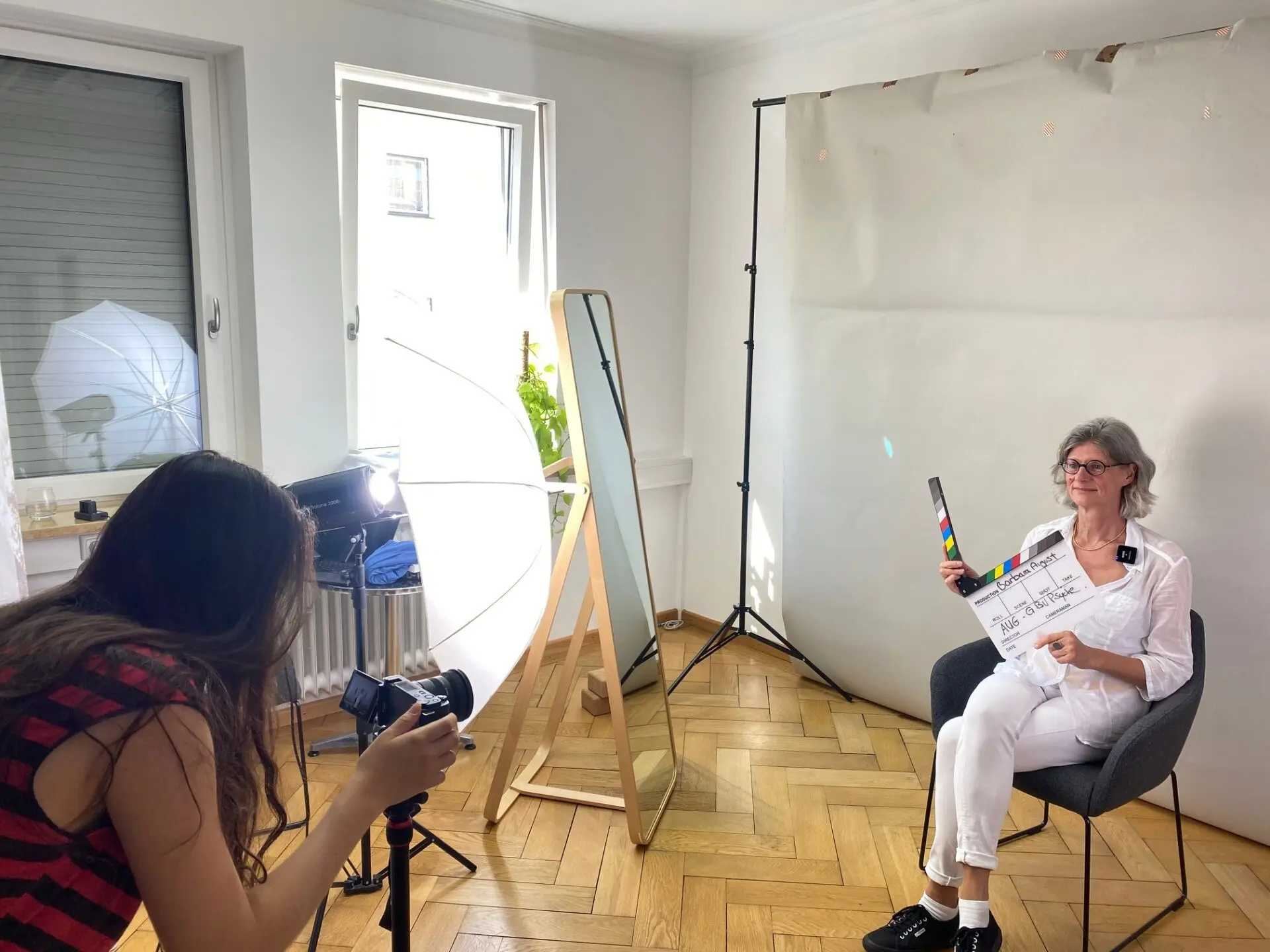 Eine Person sitzt auf einem Stuhl und hält eine Klappe während eines Video-Drehs in einem Raum.